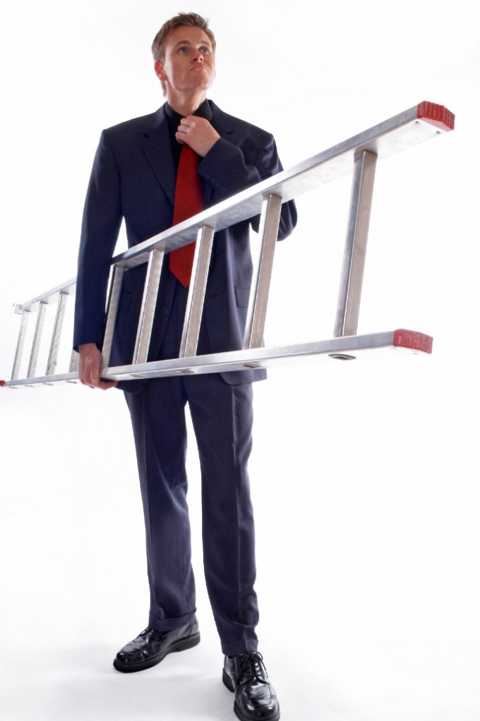 business man holding a ladder while adjusting his tie to overcome the impostor experience